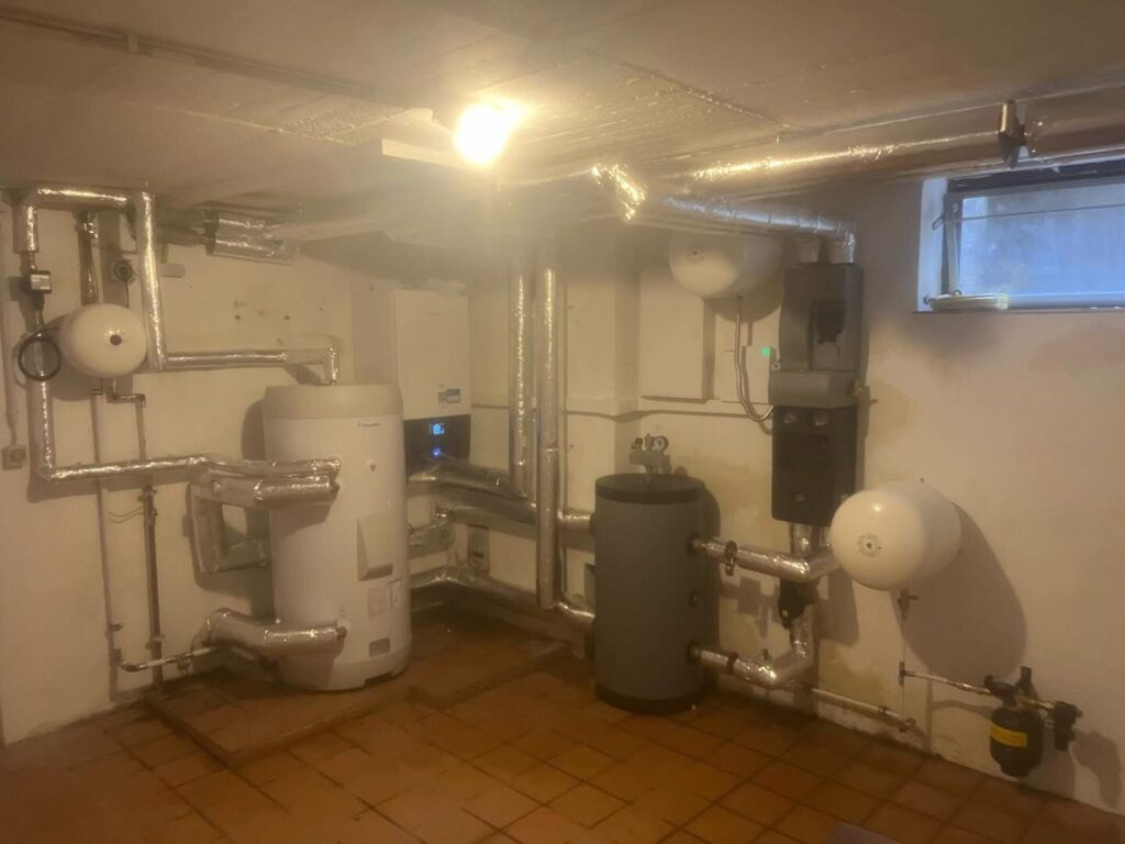 Heizung und Sanitär Köln: modernisierter Heizungsraum im Keller mit Wärmepumpen-Anlage, Warmwasserspeicher und neuen Rohrleitungen