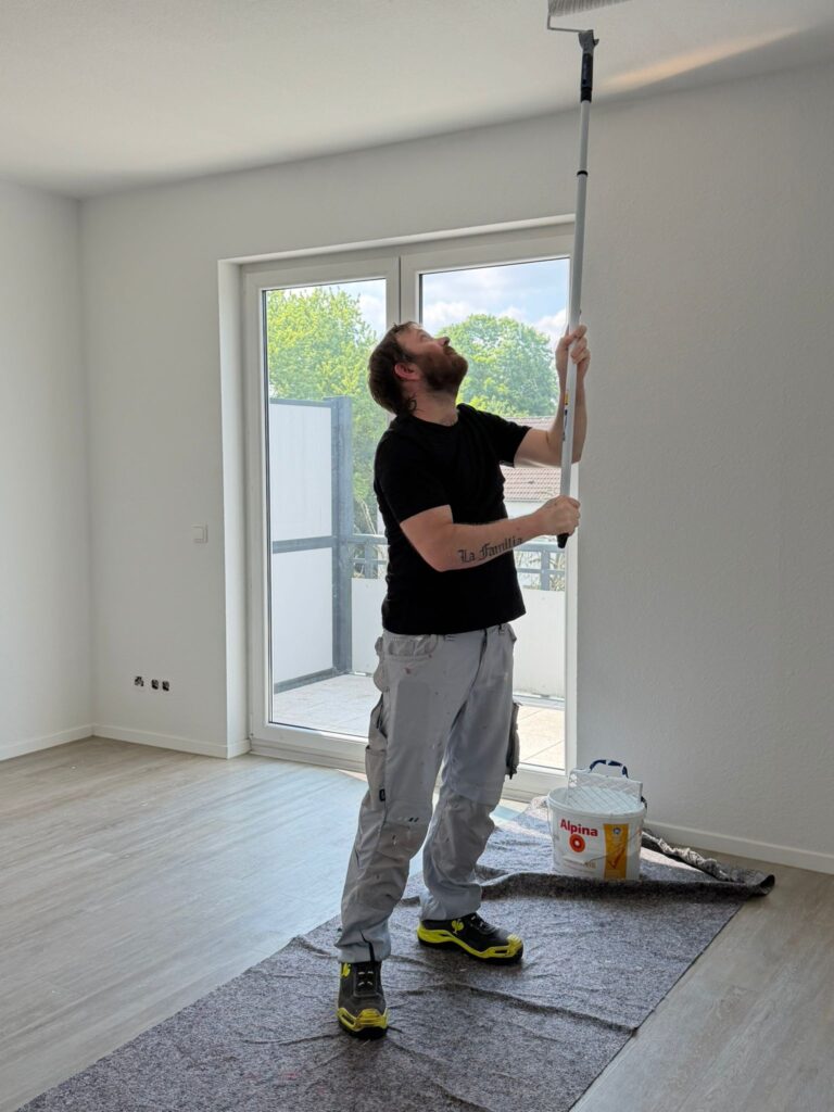Handwerkerleistungen Köln: Maler streicht die Decke einer Wohnung mit der Farbrolle – Malerarbeiten von Bones & Hammers