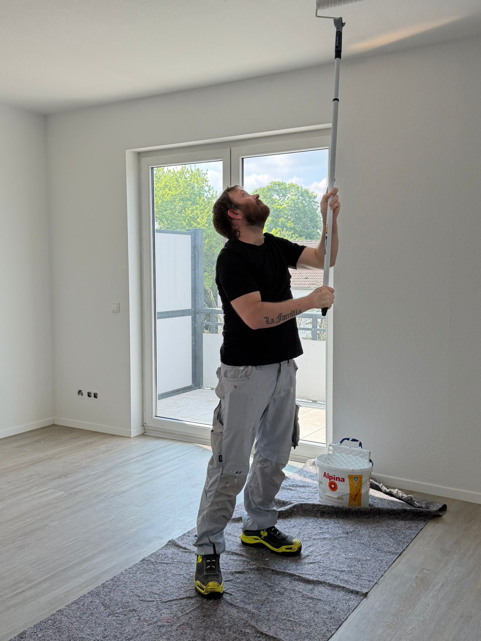 Handwerkerleistungen Köln: Maler streicht die Decke einer Wohnung mit der Farbrolle – Malerarbeiten von Bones & Hammers