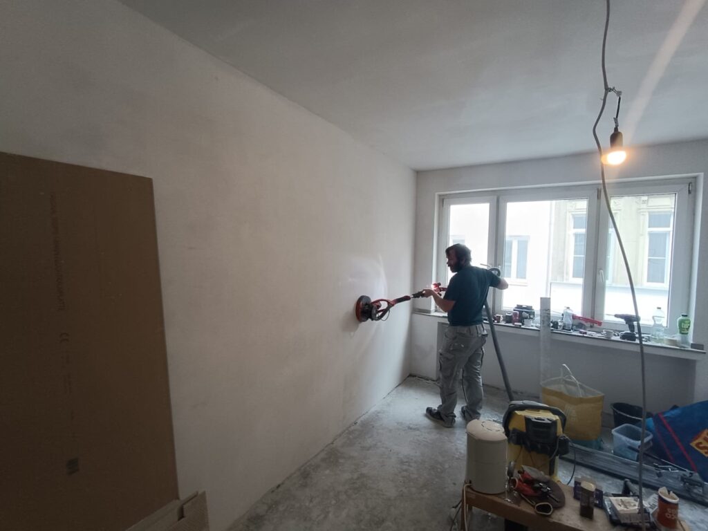 Handwerker schleift die Wände einer Wohnung mit dem Langhalsschleifer – Vorbereitung für Malerarbeiten in Köln